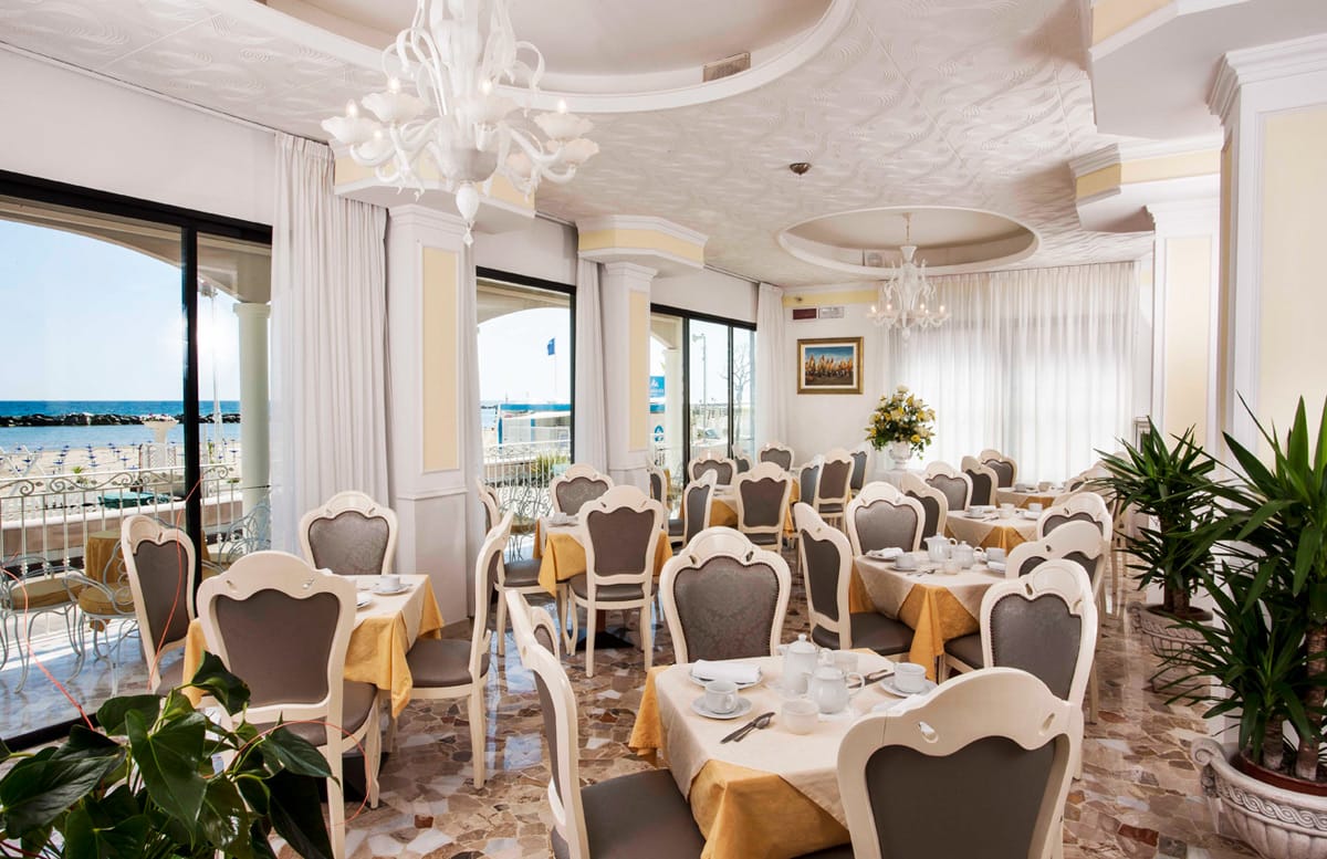 La sala del ristorante apparecchiata, con le vetrate sul mare